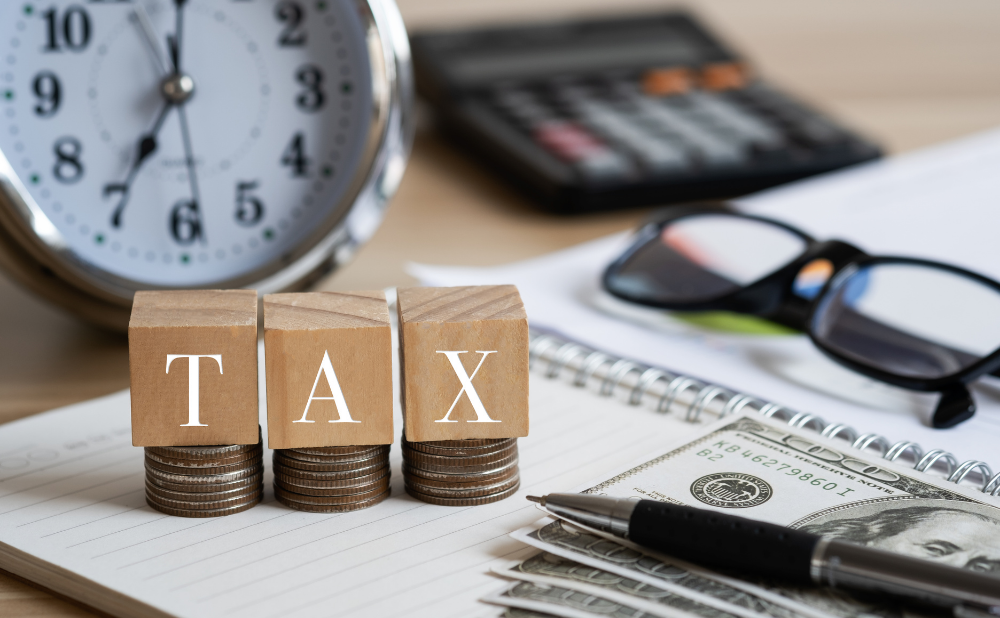 Filing the PA Inheritance Tax Return - Bumbaugh George, PLLC Blocks spelling TAX sit on coin stacks beside a clock calculator glasses and a pen over a notebook with cash nearbyillustrates taxes and accounting